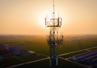 Aerial view of a 5G network communications tower, with the sun low on the horizon in the background.
