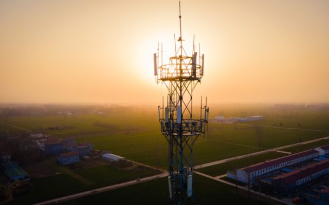 Aerial view of a 5G network communications tower, with the sun low on the horizon in the background.