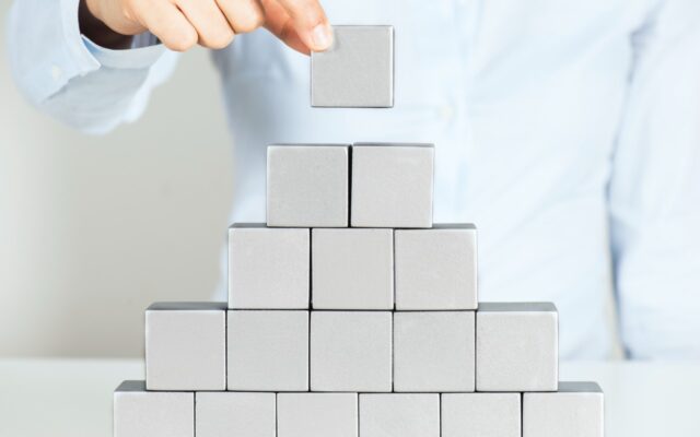 Woman building a pyramid wall with gray or silver cubes.
