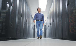 Man walking down aisle between rows of servers in data center. 