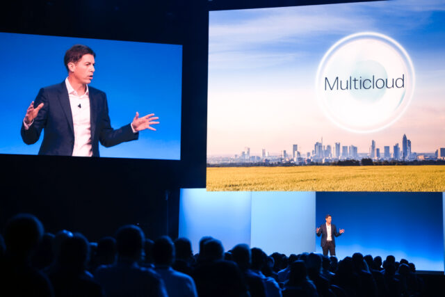 Chuck Whitten, Dell Technologies Co-COO appears on stage at the 2023 Dell Technologies World Day One Keynote, as a video screen shows him on the left and graphic about multicloud appears on adjacent video screen on right. 