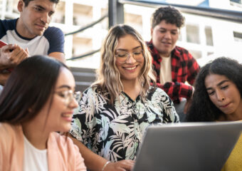 Young woman showing something on the laptop to her friends on university stairs