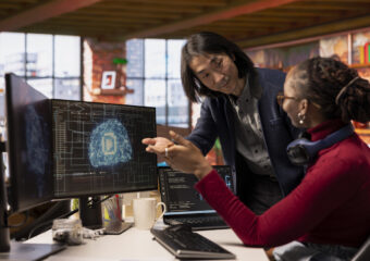 CTO manager in multiethnic startup office helps technician coding advanced AI algorithm and machine learning models. Team leader overseeing work done by employee in Silicon Valley workplace