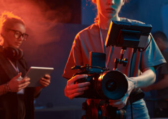 Cropped shot of female cameraman operating equipment in studio set with neon lights copy space